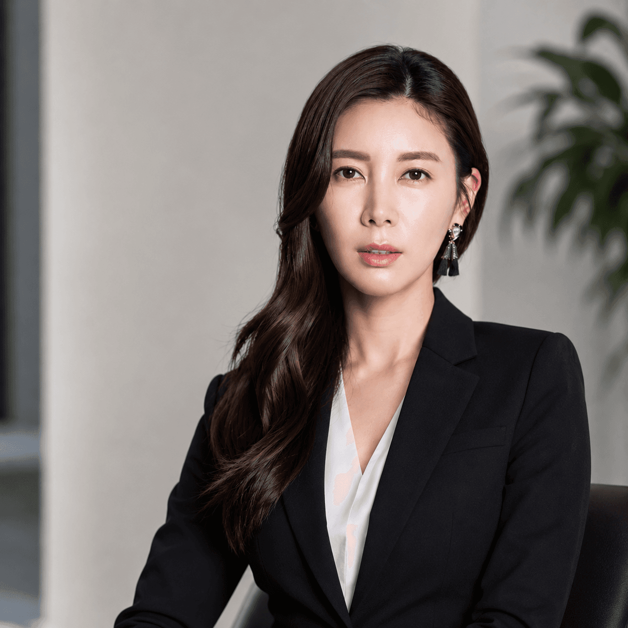 Professional woman with long dark hair wearing a black blazer and white blouse, looking forward.